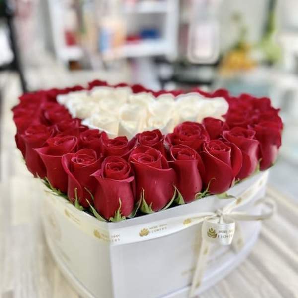 Heart-shaped white box filled with red roses around a cluster of white roses in the center