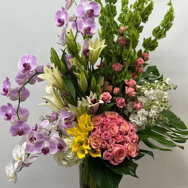 Tall mixed bouquet with orchids, roses, lilies, and hydrangeas in a glass vase