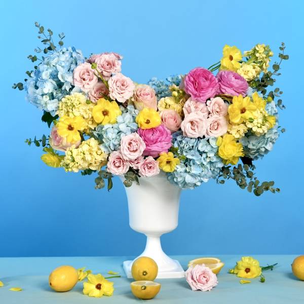 Colorful mixed bouquet in a white pedestal vase with lemons on the table