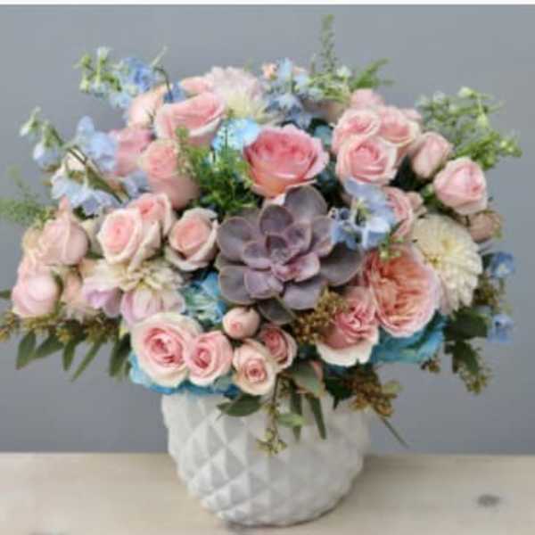 Pink roses and blue flowers arranged in a white vase with a succulent center