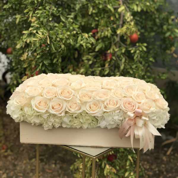 Cream roses arranged over white hydrangeas in a rectangular box with a ribbon bow
