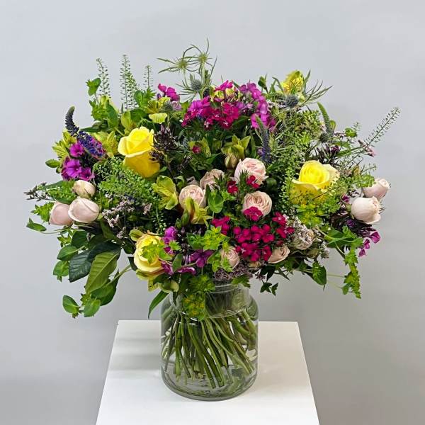 Mixed bouquet of yellow, pink, and purple flowers in a glass vase