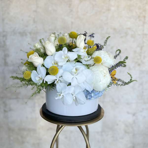 White orchids and roses in a round white vase with yellow accents