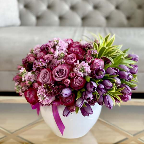 Pink and purple flower arrangement in a white vase with a ribbon