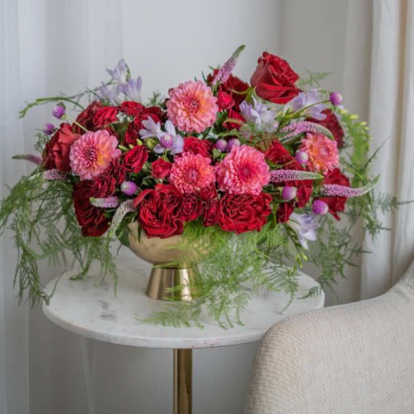 Red and pink floral arrangement in a gold vase