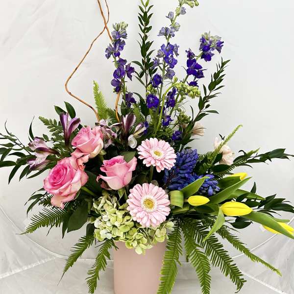 Mixed bouquet of pink roses, lilies, and purple flowers in a pink vase