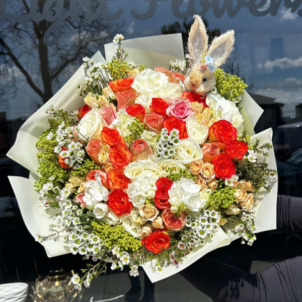 Large bouquet of red, white, and peach roses with a small bunny topper