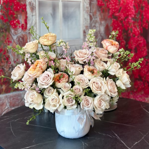 Cream and blush roses arranged in a white vase with a ribbon