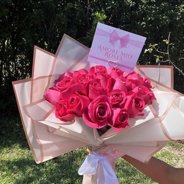 Bouquet of bright pink roses wrapped in blush paper with a white ribbon