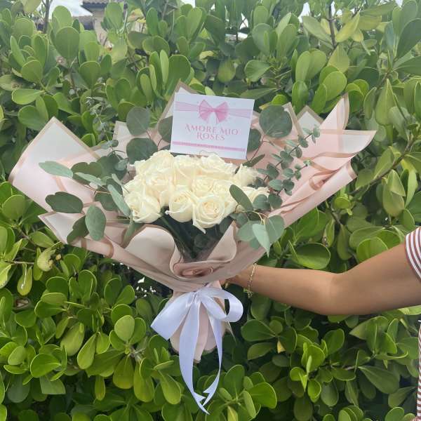 Bouquet of cream roses wrapped in blush paper with a white ribbon