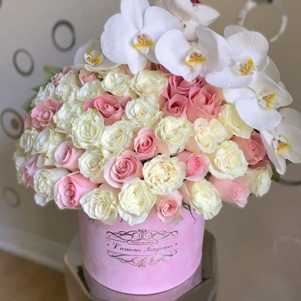 Round box arrangement of white orchids and pink and cream roses in a pink hatbox.