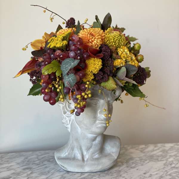 Autumn floral arrangement in a silver bust vase with grapes and yellow blooms