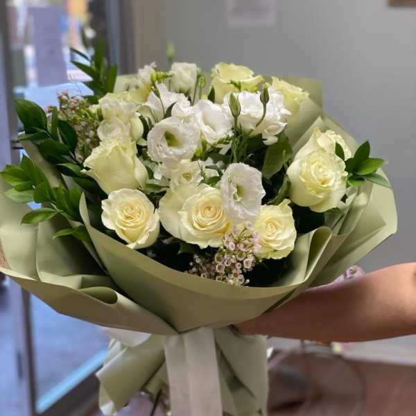 Bouquet of white and pale yellow roses with white blooms wrapped in sage paper