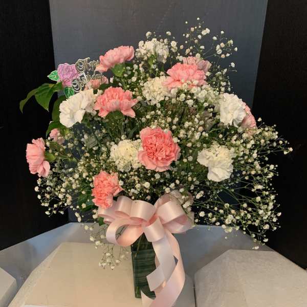 Pink and white carnations with baby's breath in a vase, tied with a pink ribbon