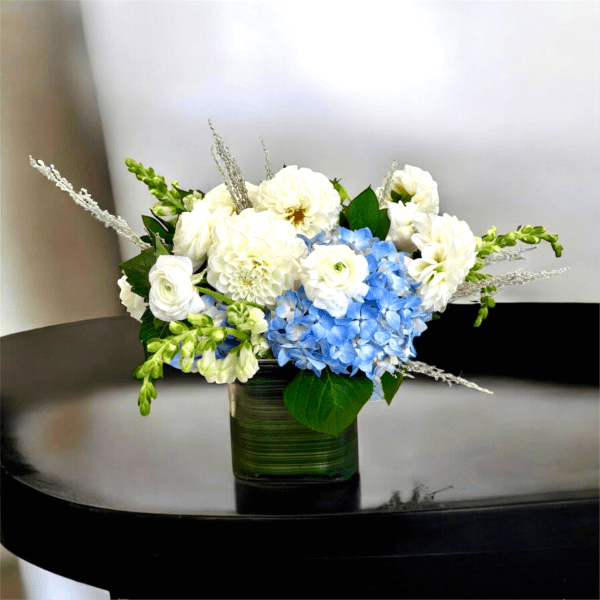 Blue and white floral arrangement in a green glass vase