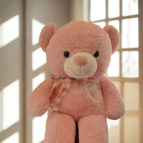 Pink teddy bear with a plaid ribbon sitting indoors
