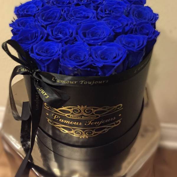 Round black hat box filled tightly with vivid blue roses and tied with a black ribbon