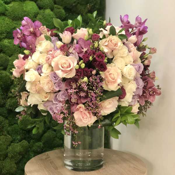 Large arrangement of pink, white, and purple roses with orchids in a clear glass vase