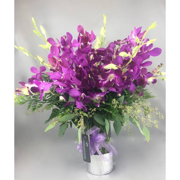 Purple orchid arrangement in a white vase with a ribbon