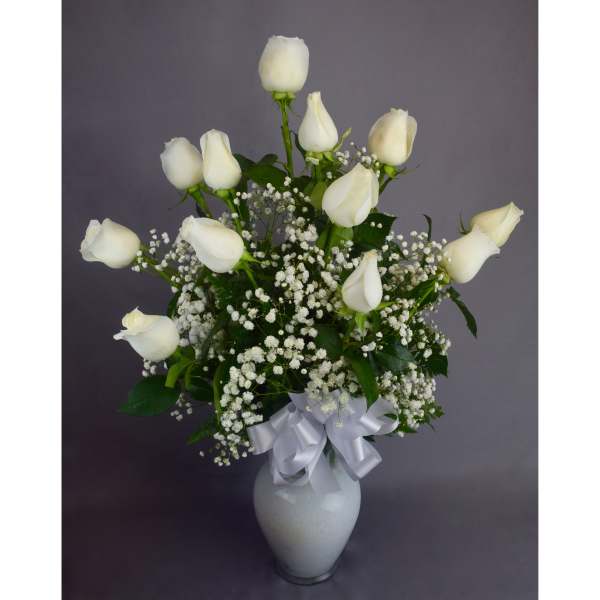 White roses arranged in a white vase with baby's breath and a white ribbon