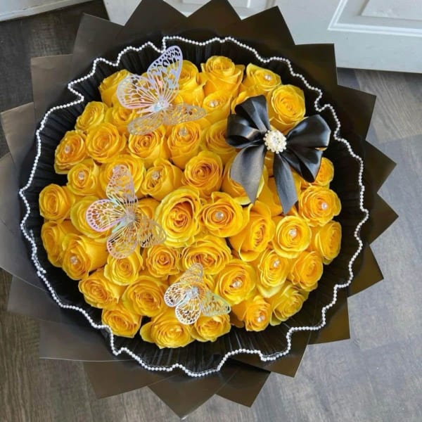 Bouquet of yellow roses wrapped in black paper with butterfly accents