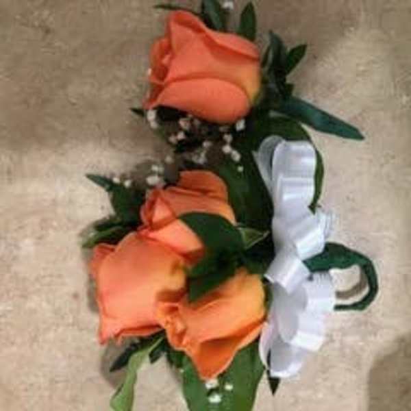 Orange rose corsage with white ribbon on a beige background