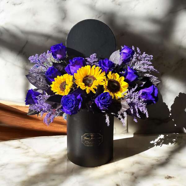 Purple roses and yellow sunflowers in a black hatbox
