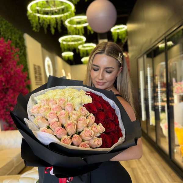 Large bouquet of pink, cream, and red roses wrapped in black paper