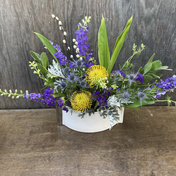 Low floral arrangement with purple and yellow blooms in a white container