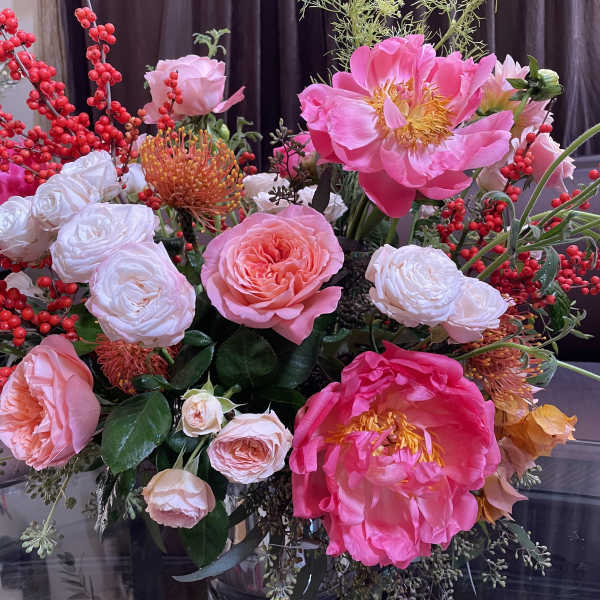 Pink and white floral arrangement with red berry branches in a glass vase