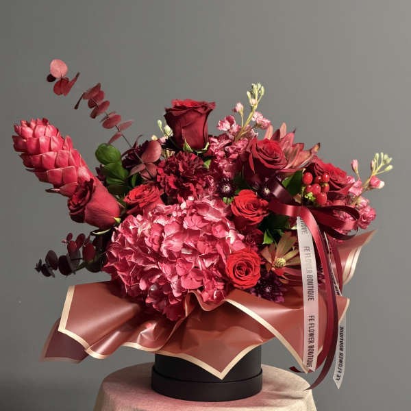 Red and pink floral arrangement in a round black box with ribbon