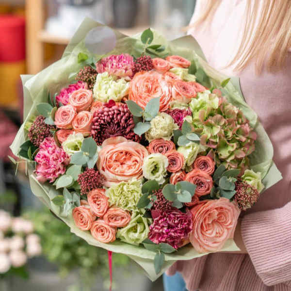Bouquet of peach, pink, and green flowers wrapped in pale paper