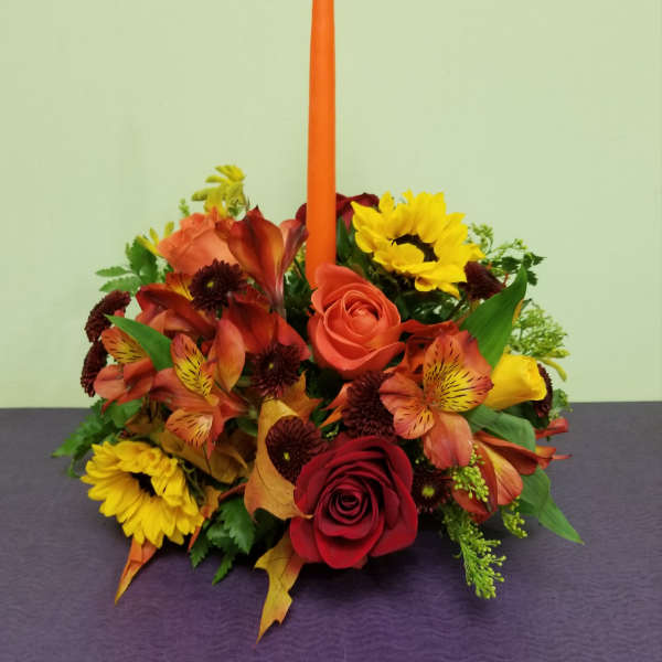 Autumn floral centerpiece with roses, sunflowers, and a tall orange candle