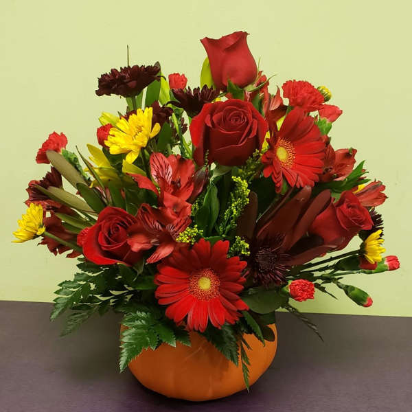 Red and yellow mixed flower arrangement in an orange pumpkin vase