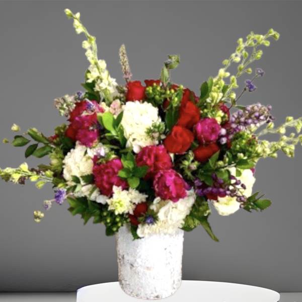 Mixed bouquet of red, pink, and white flowers in a white vase
