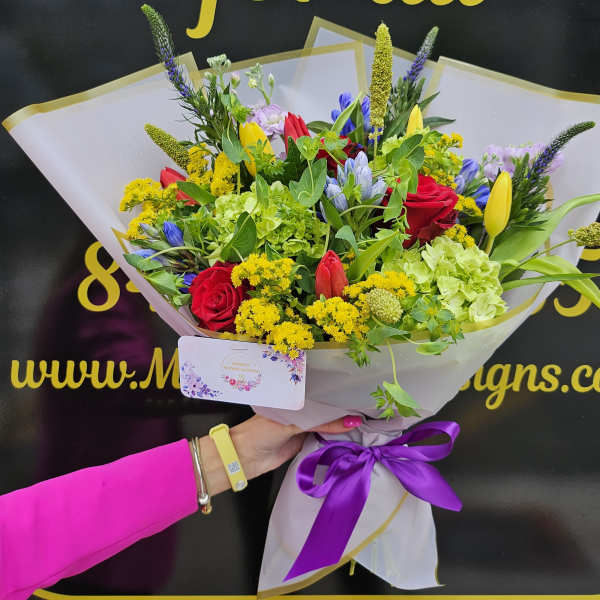 Bouquet of red roses, yellow tulips, and green hydrangeas wrapped in white paper