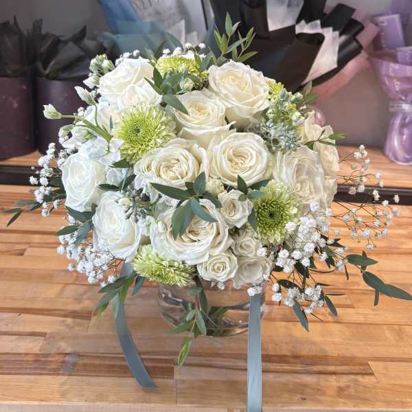 White roses and green chrysanthemums in a glass vase with trailing ribbon.