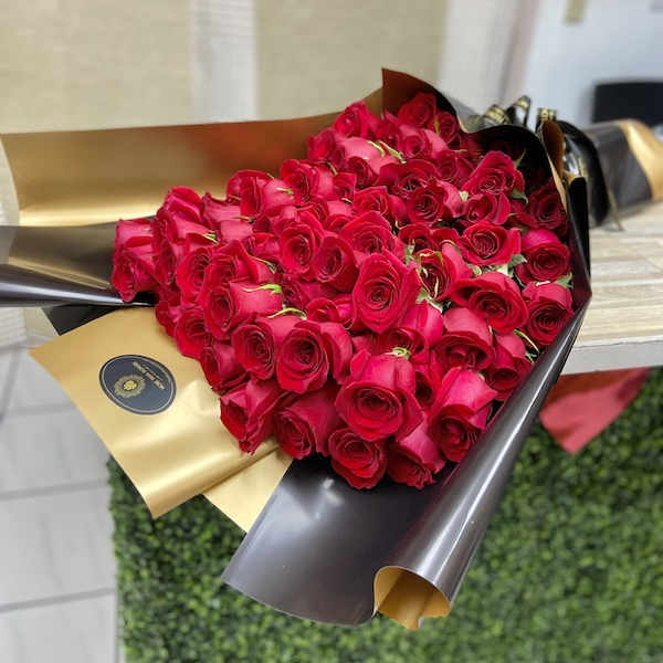 Large bouquet of tightly clustered red roses wrapped in glossy black and gold paper