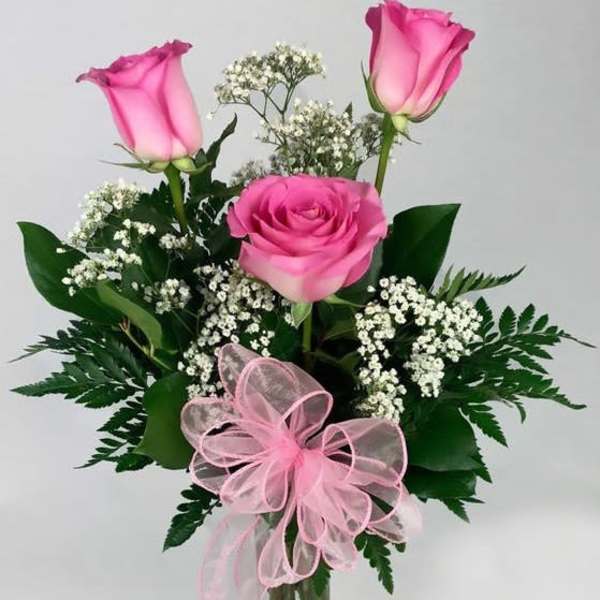 Pink roses in a clear glass vase with baby's breath and a pink ribbon bow