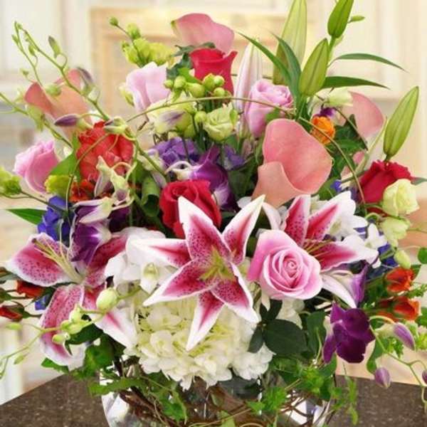 Mixed bouquet of pink lilies, roses, and orchids in a glass bowl vase