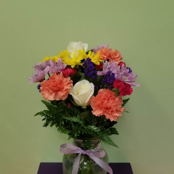 Mixed bouquet of carnations, daisies, and roses in a glass vase with a ribbon