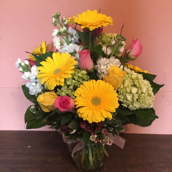 Bouquet of yellow gerbera daisies, pink roses, and white blooms in a glass vase
