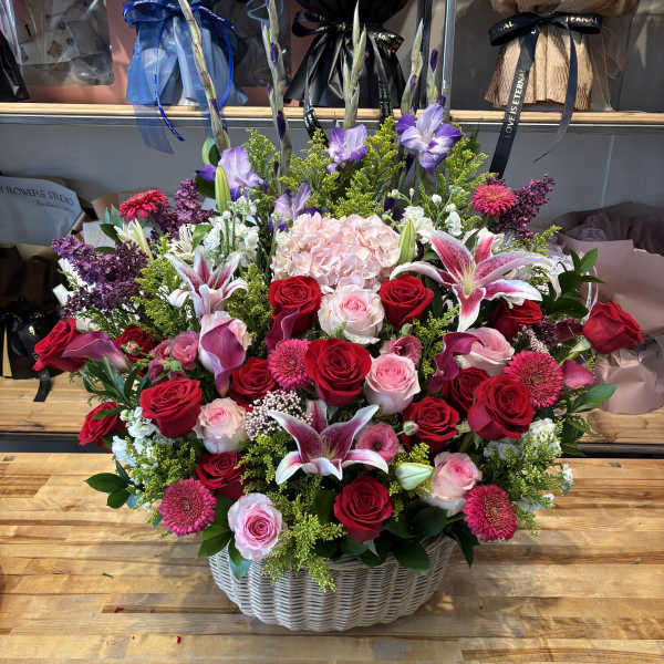Large basket arrangement of red and pink roses with lilies and purple flowers