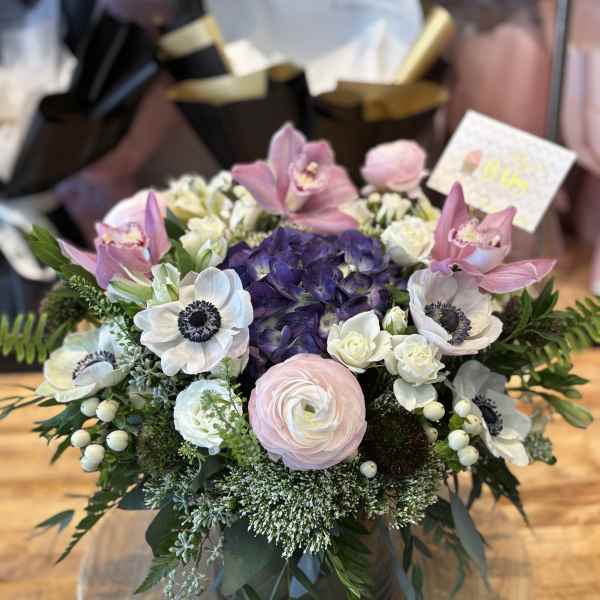 Round bouquet with pink orchids, white anemones, and purple hydrangea in a vase