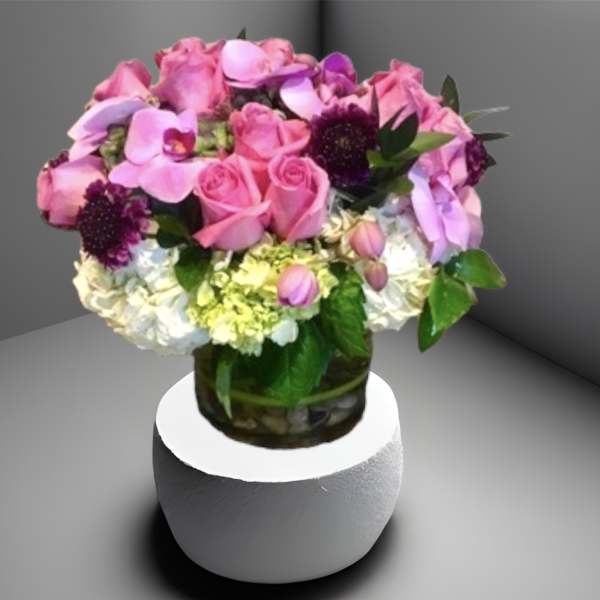 Pink and purple bouquet in a glass vase on a white pedestal