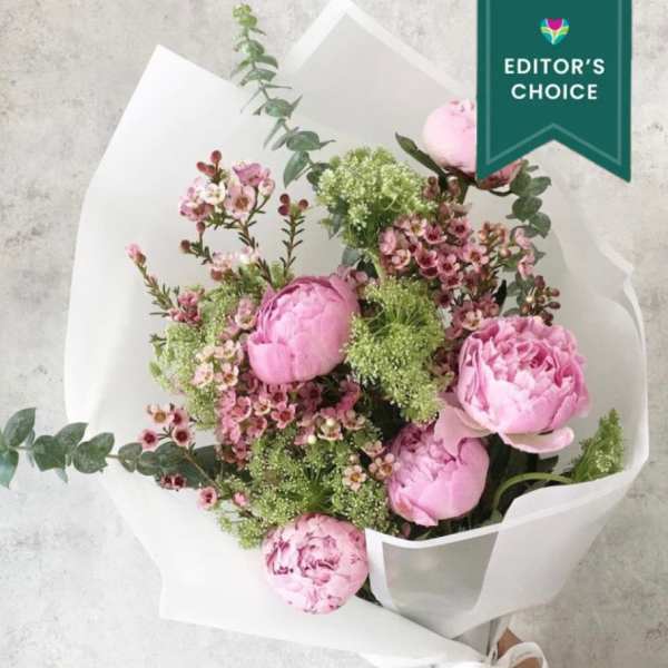 Pink peony bouquet with small filler flowers in white wrapping
