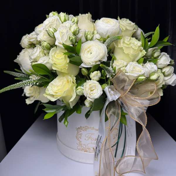 White rose and ranunculus arrangement in a round hatbox with ribbon