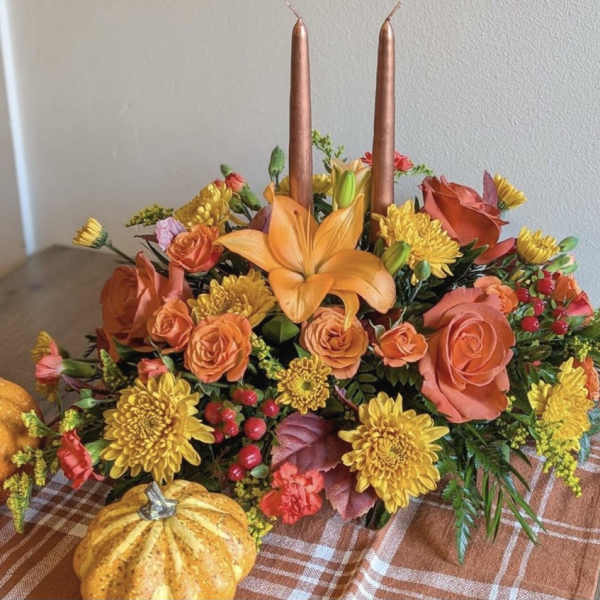 Autumn floral centerpiece with orange lilies, roses, and yellow mums around two candles
