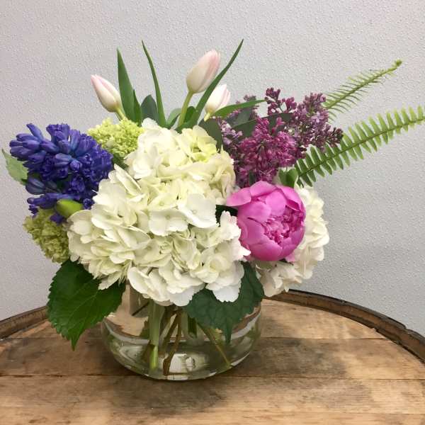 Mixed bouquet in a clear glass vase with white hydrangeas, pink peony, and purple blooms