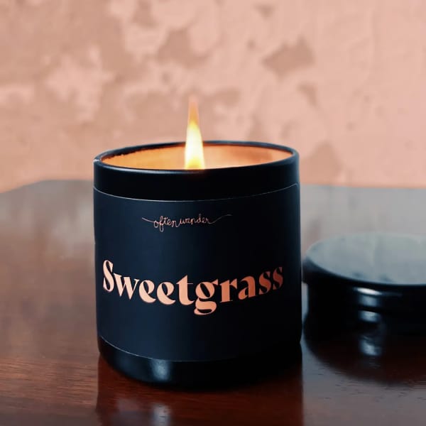 Lit black candle in a jar labeled Sweetgrass
